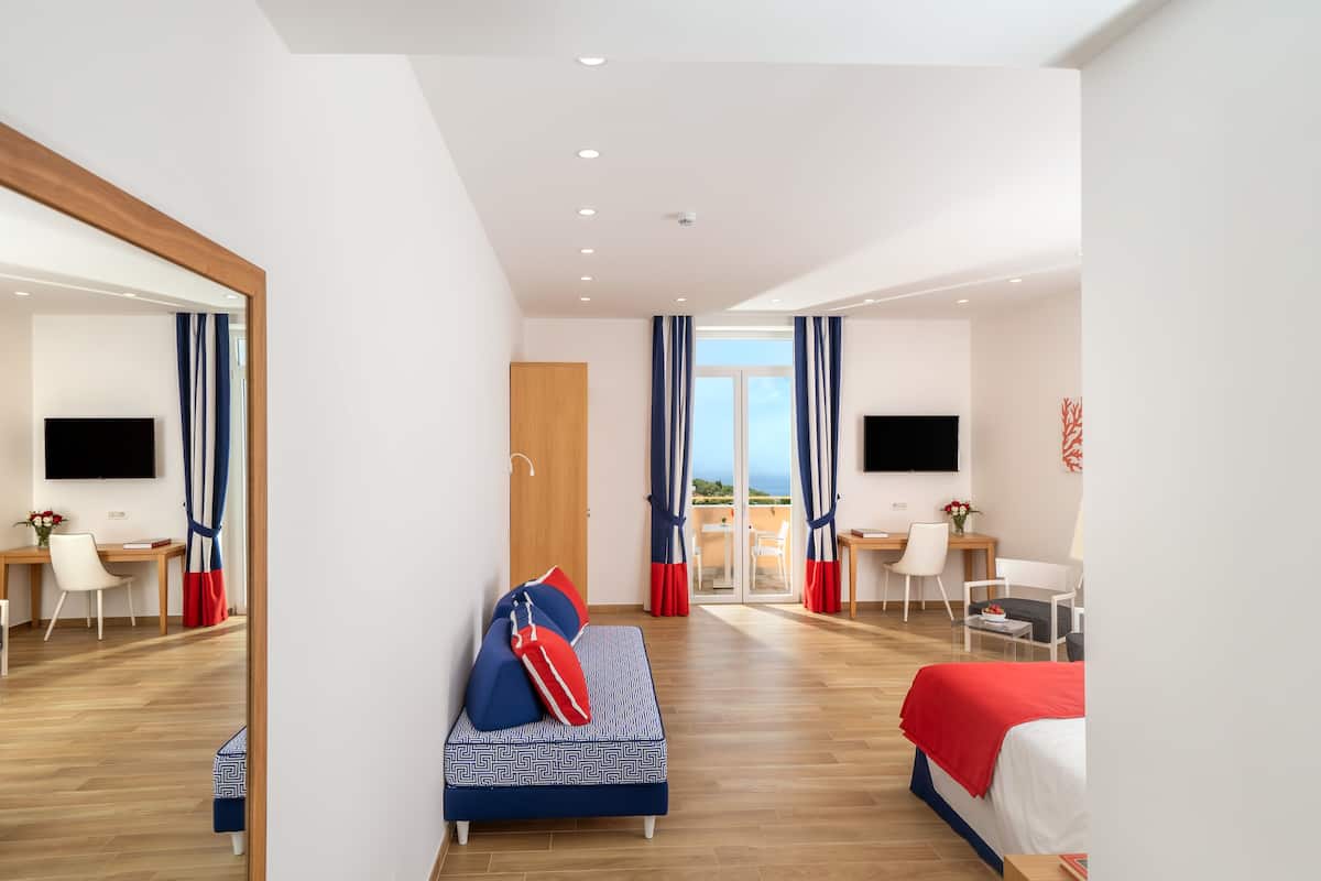 A modern hotel room with a bed, a sofa, a desk, and a TV.