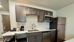 A compact kitchen with a microwave, refrigerator, and dishwasher. There is a small dining area with a table and chairs. - Alaska's Select Inn Wasilla (Wasilla)
