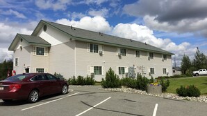 A multi-story hotel with a parking lot, air conditioning units, and a flag on the building. - Alaska's Select Inn Wasilla (Wasilla)