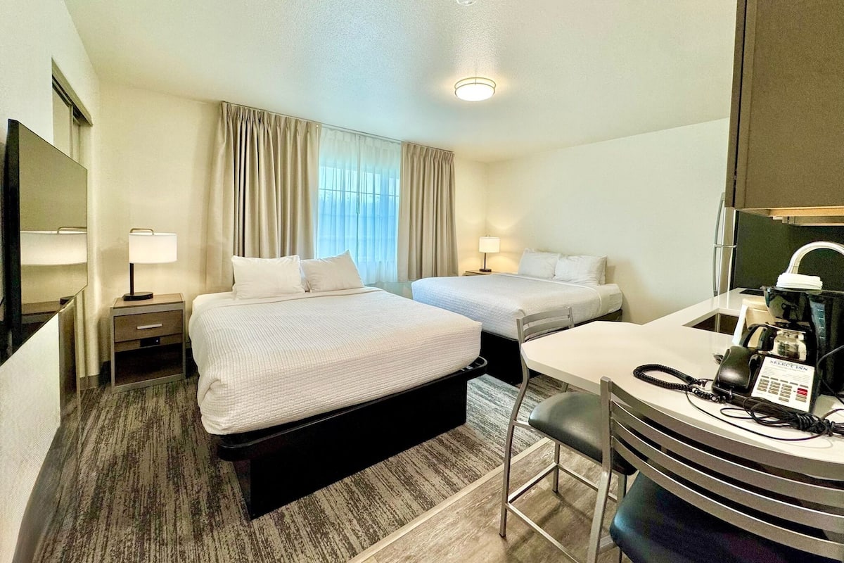 A hotel room with two beds, a desk with a telephone, and a mirror.