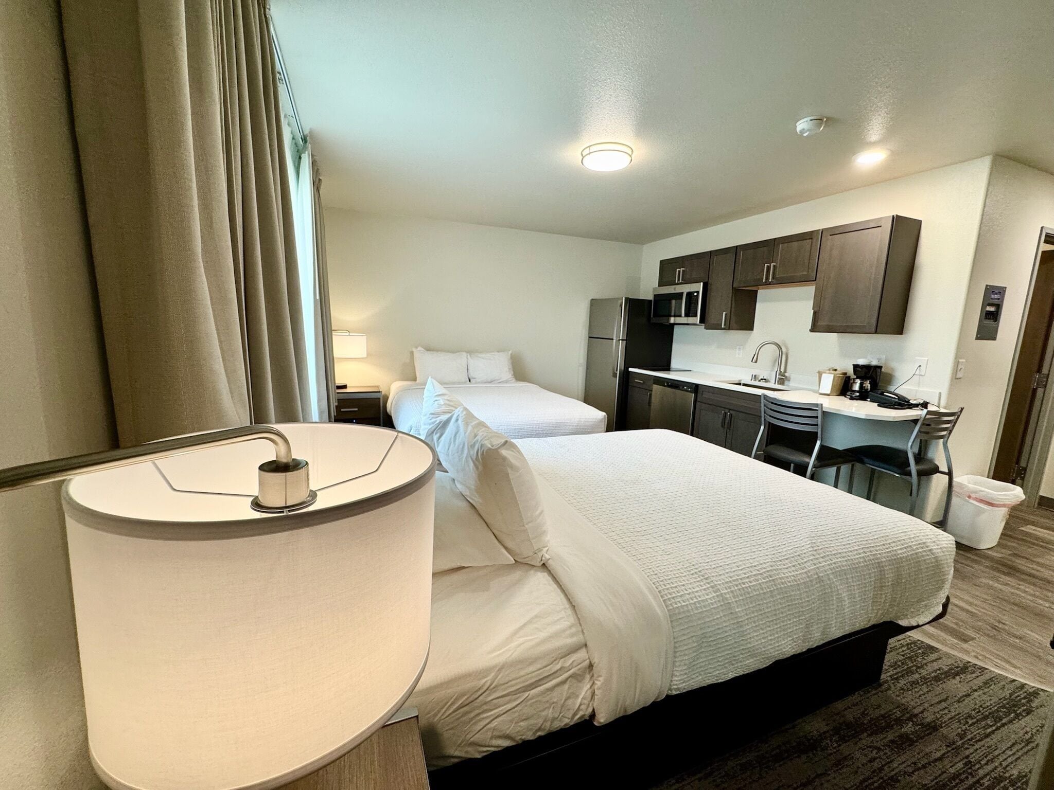 A hotel room with a bed, a desk, a kitchenette, and a bathroom.
