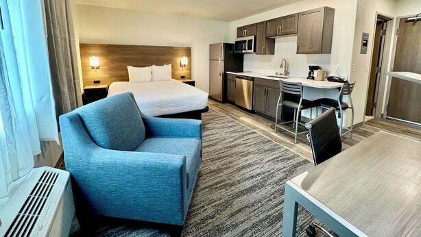 A hotel room with a bed, a blue armchair, a dining table, a kitchen area with a microwave, and a refrigerator. - Alaska's Select Inn Wasilla (Wasilla)