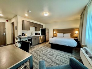 A hotel room with a bed, a desk, a microwave, a refrigerator, and a seating area.