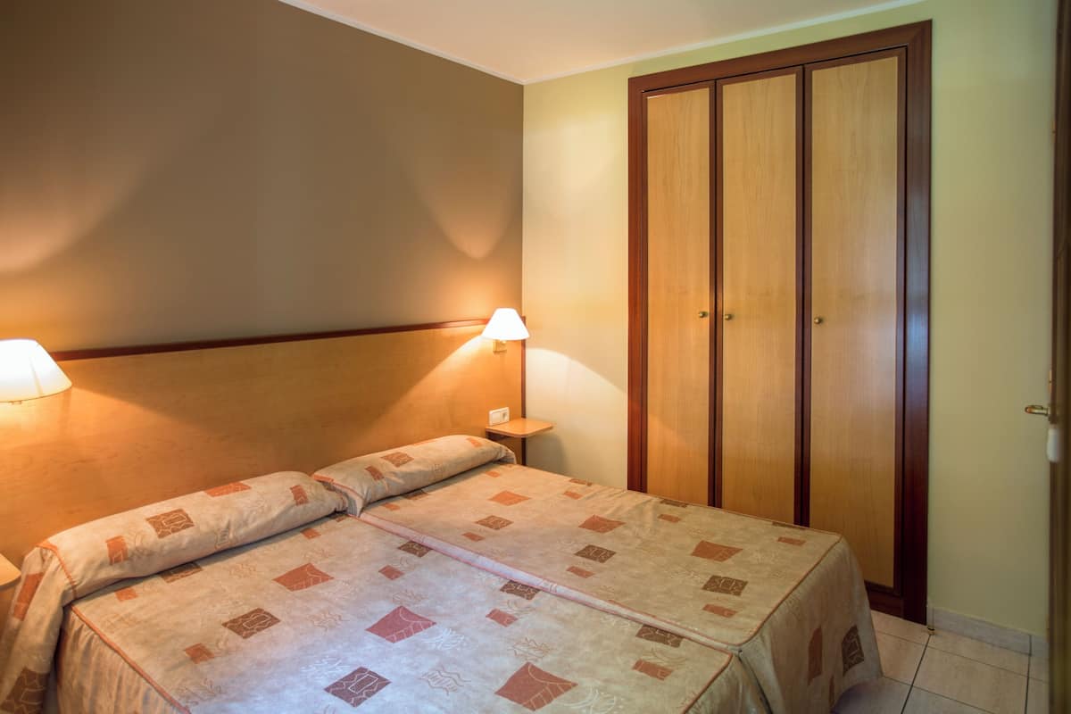 A hotel room with a bed, bedside lamps, a wooden wardrobe, and a small bedside table.