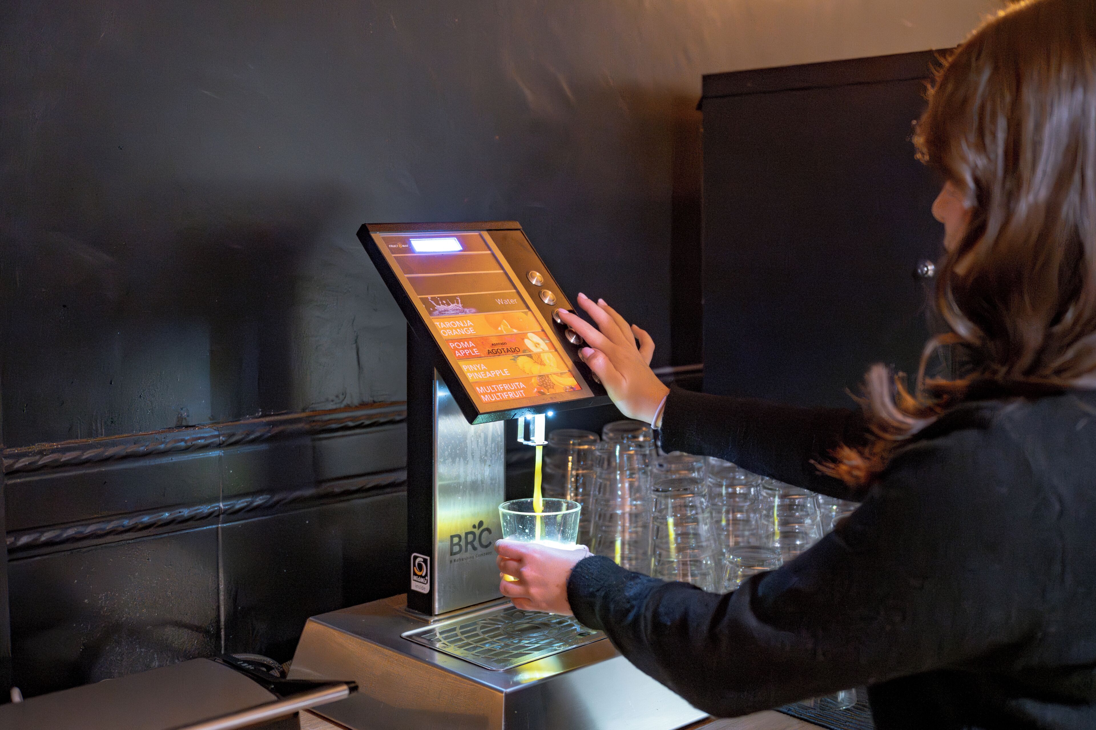 Eine Person bedient einen Getränkeautomaten mit Touchscreen und füllt ein Getränk in eine Tasse.