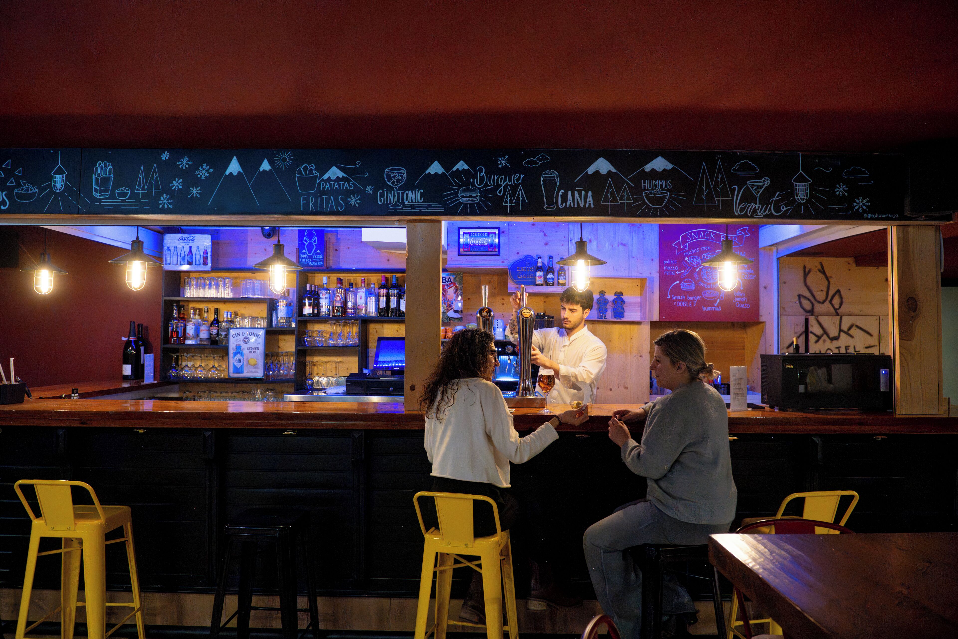 A bar with a chalkboard menu, bar stools, and a counter where a bartender is serving drinks.
