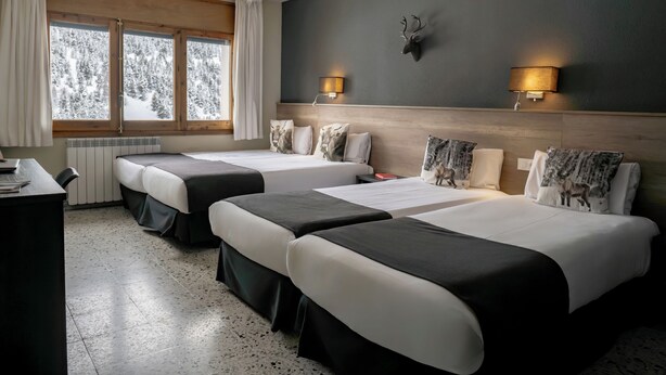 Habitación de hotel con dos camas, cabecera de madera, cabeza de ciervo montada en la pared y ventana con vistas a árboles.
