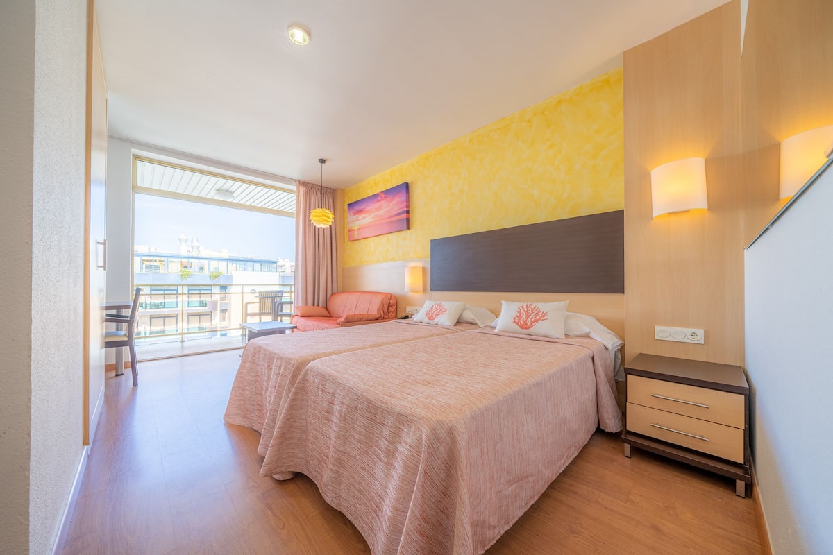 A hotel room with two beds, a balcony, and a view of the city.