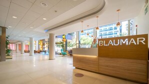 A modern hotel lobby with a wooden reception desk, large windows, and hanging pendant lights. - Blaumar (Blanes)