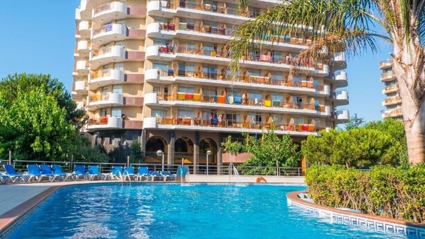 A multi-story hotel with balconies, a swimming pool, and lush greenery. - Blaumar (Blanes)