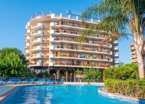 Un hotel de varios pisos con balcones, piscina y abundante vegetación.
