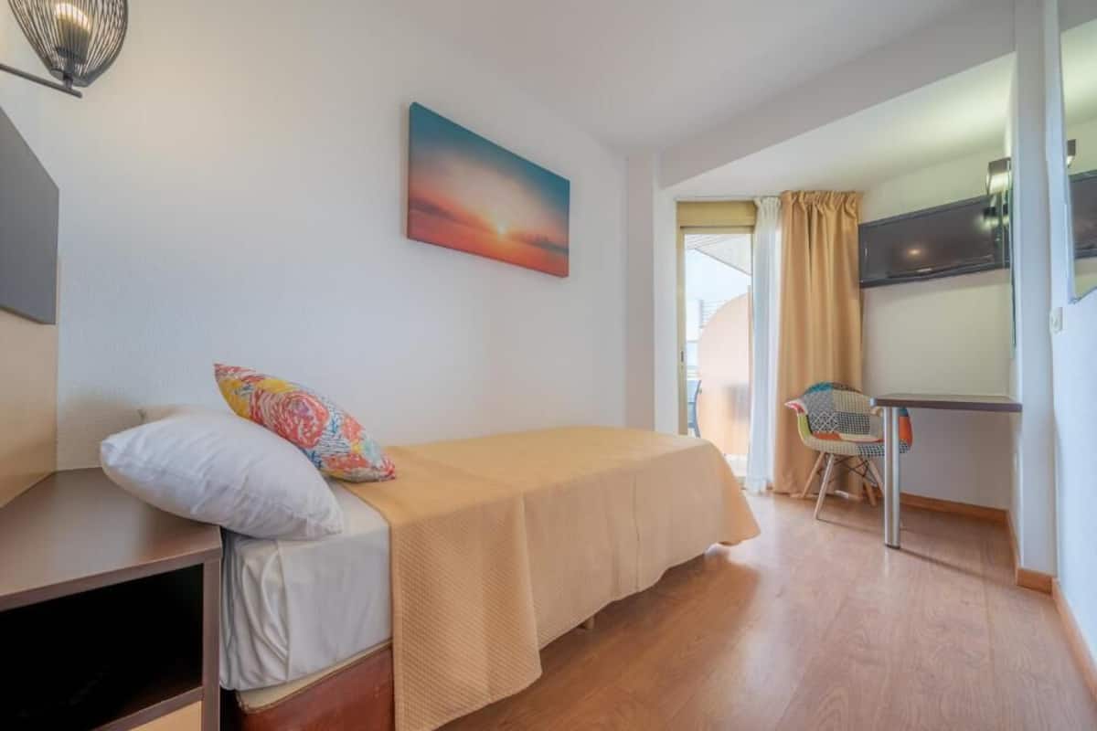 A bedroom with a bed, a desk, a chair, and a painting on the wall.