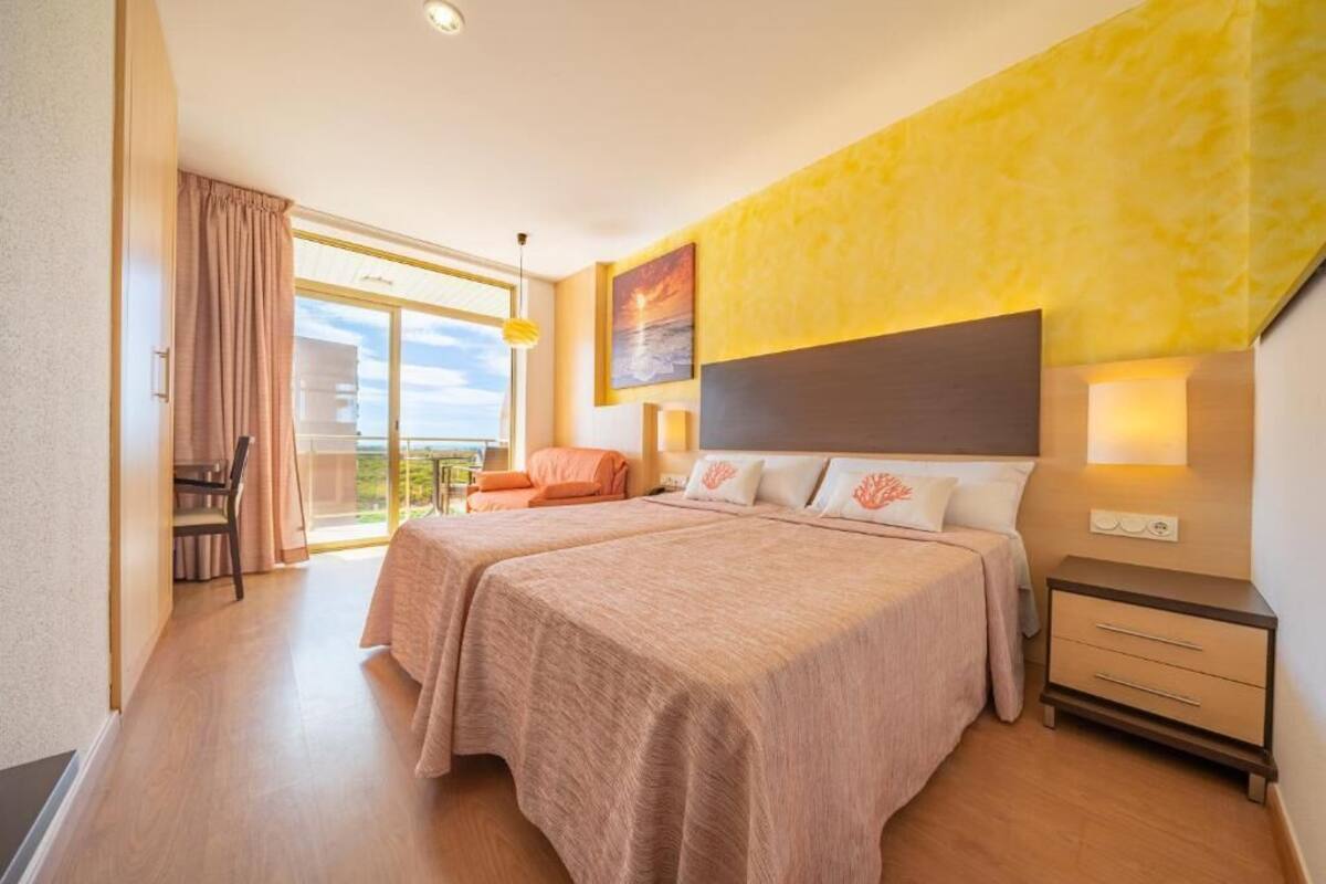 A hotel room with two beds, a balcony, and a view of the sky.