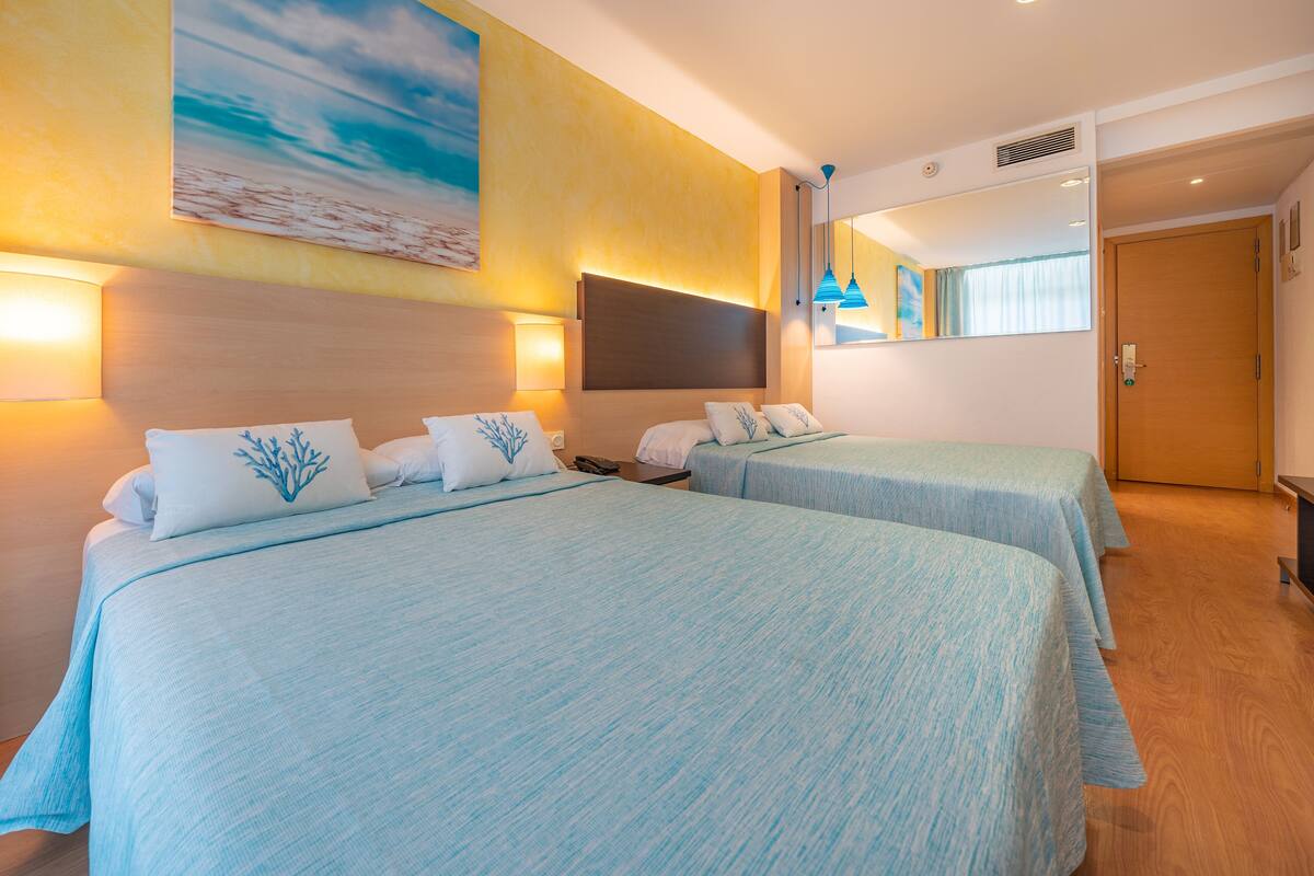 A hotel room with two beds, a large painting on the wall, and a wooden door.