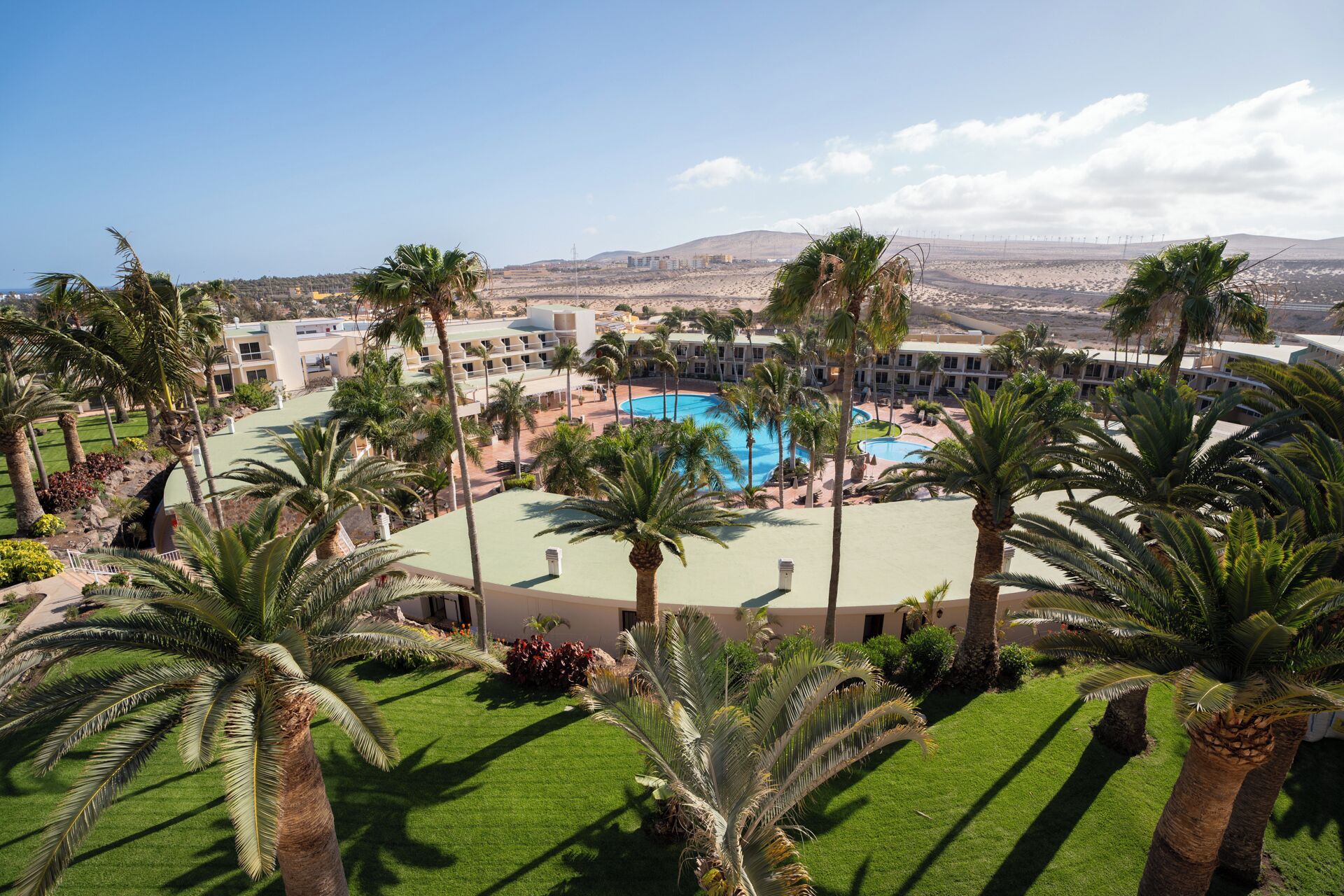 A resort with a central pool, palm trees, and a view of distant mountains.