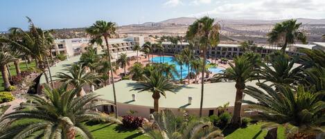 A resort with a central pool, palm trees, and a view of distant mountains.