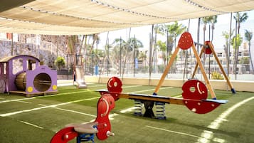 Un parque infantil con un sube y baja, una estructura para escalar y un tobogán.
