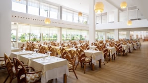 A spacious dining area with multiple tables and chairs, large windows, and hanging light fixtures. - Hotel Drago Park by Pierre & Vacances (Pajara)