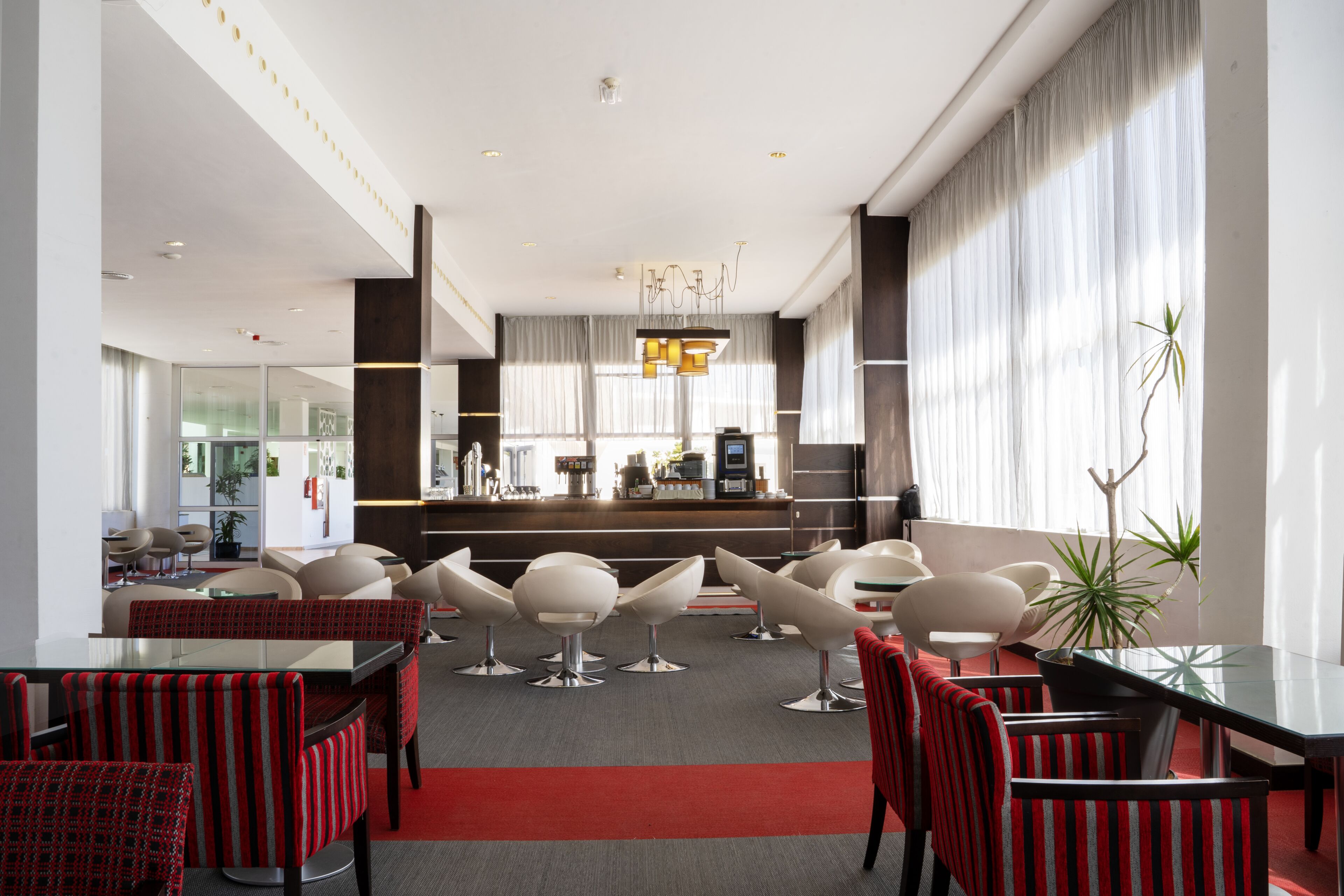 En modern hotellobby med en bardisk, sittgrupper och ett stort fönster som släpper in naturligt ljus.