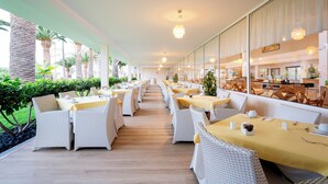 A restaurant with long tables and wicker chairs, a wooden floor, and a view of the outdoor garden. - Hotel Drago Park by Pierre & Vacances (Pajara)