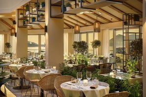 Een restaurant met ronde tafels, rieten stoelen en potplanten.
