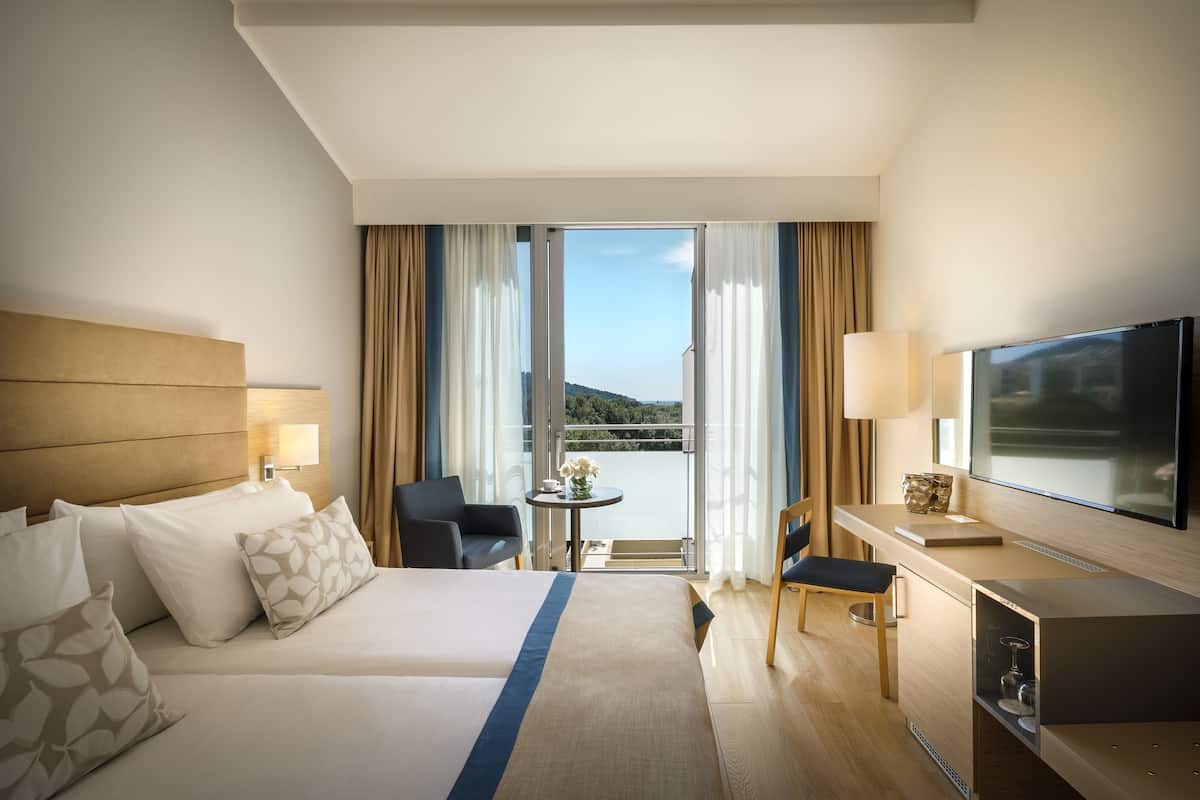 A hotel room with a bed, a desk, a TV, and a balcony with a view.