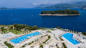 A resort with two large swimming pools, a landscaped area with lounge chairs, and a view of the sea and a small island.