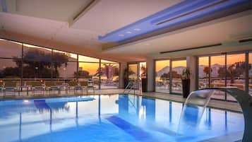 Piscina interna com paredes de vidro transparente, vista para o pôr do sol e design arquitetônico moderno.