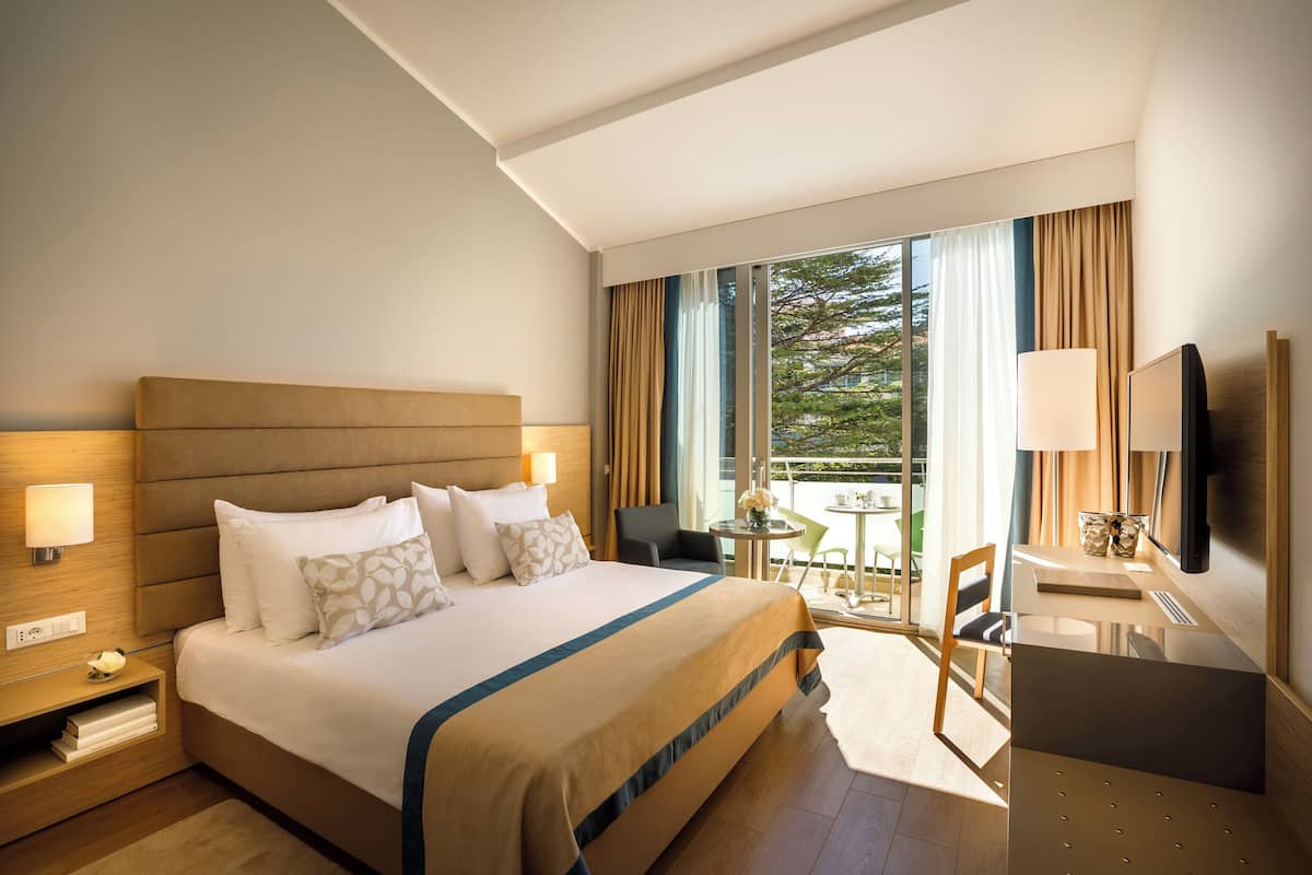 A hotel room with a large bed, bedside tables, a desk, a chair, and a TV.