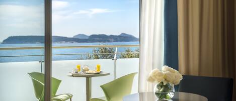 Un balcon avec une table et des chaises, un vase rempli de fleurs et une vue sur la mer et le paysage lointain.
