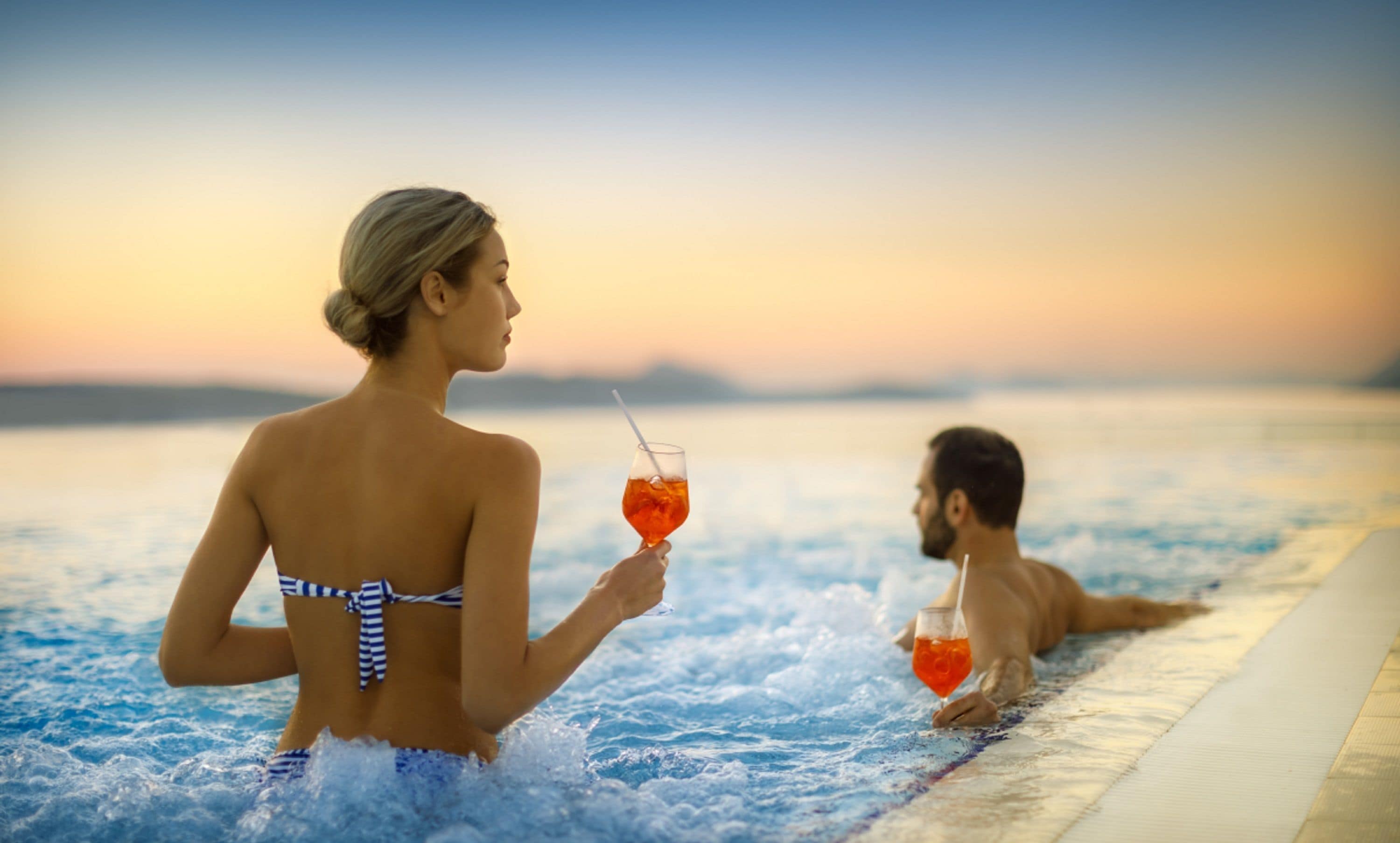 A couple relaxing in a hot tub with a sunset view.