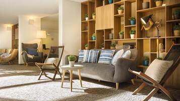 A cozy living room with a grey sofa, wooden shelves with plants, a small round table, and a floor lamp.
