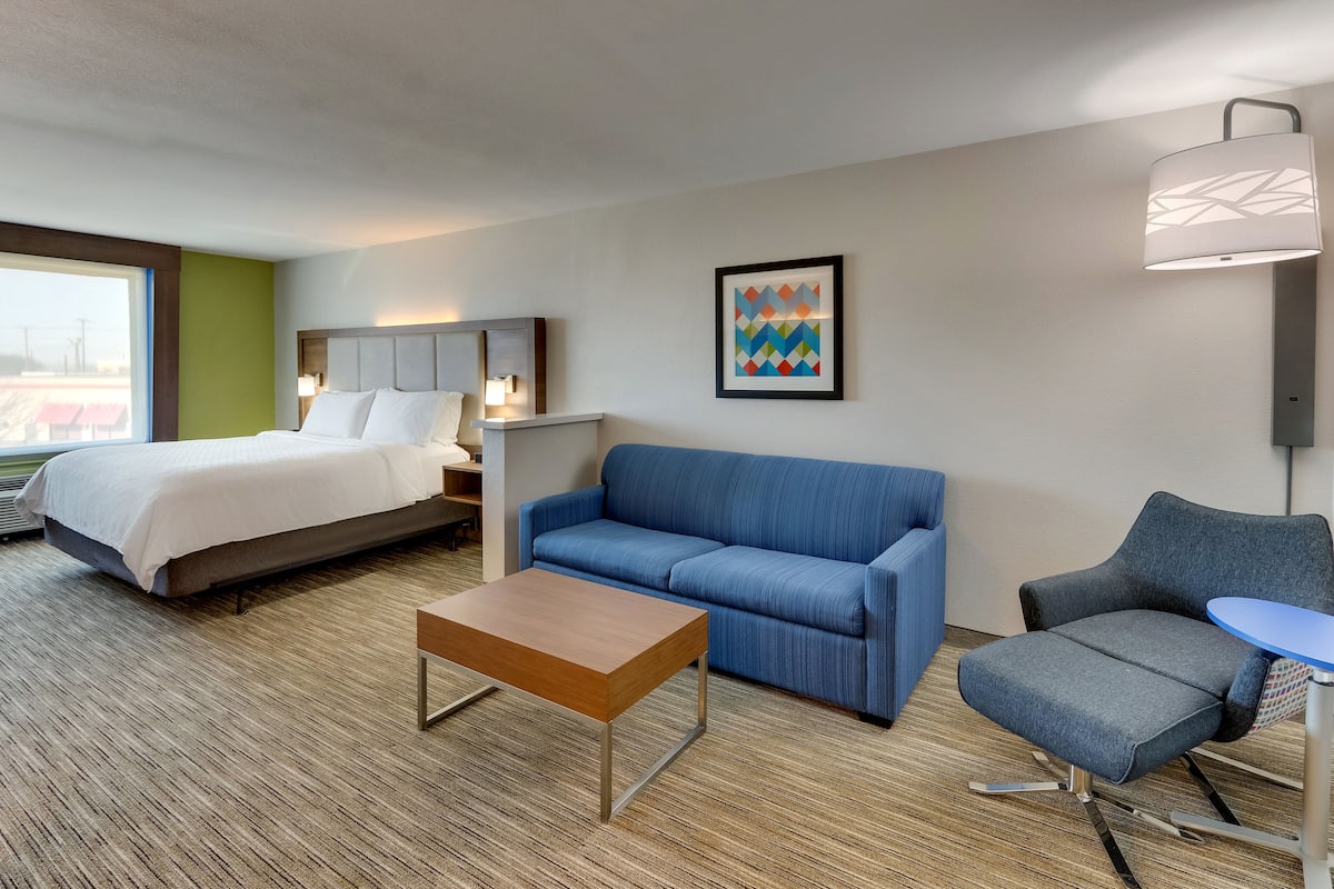 A hotel room with a bed, a blue sofa, a small table, and a chair.
