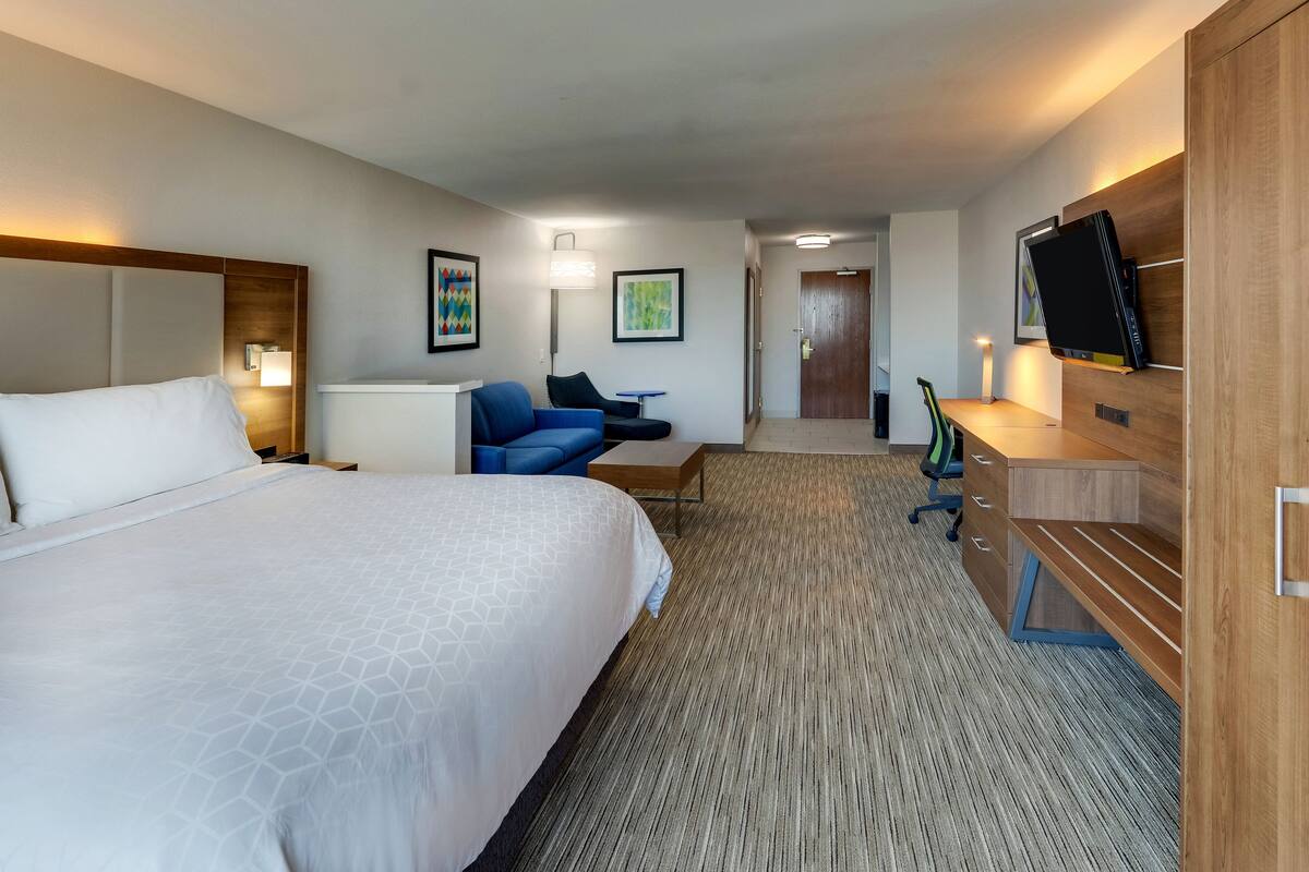 A hotel room with a large bed, a desk, a chair, a TV, and a wardrobe.