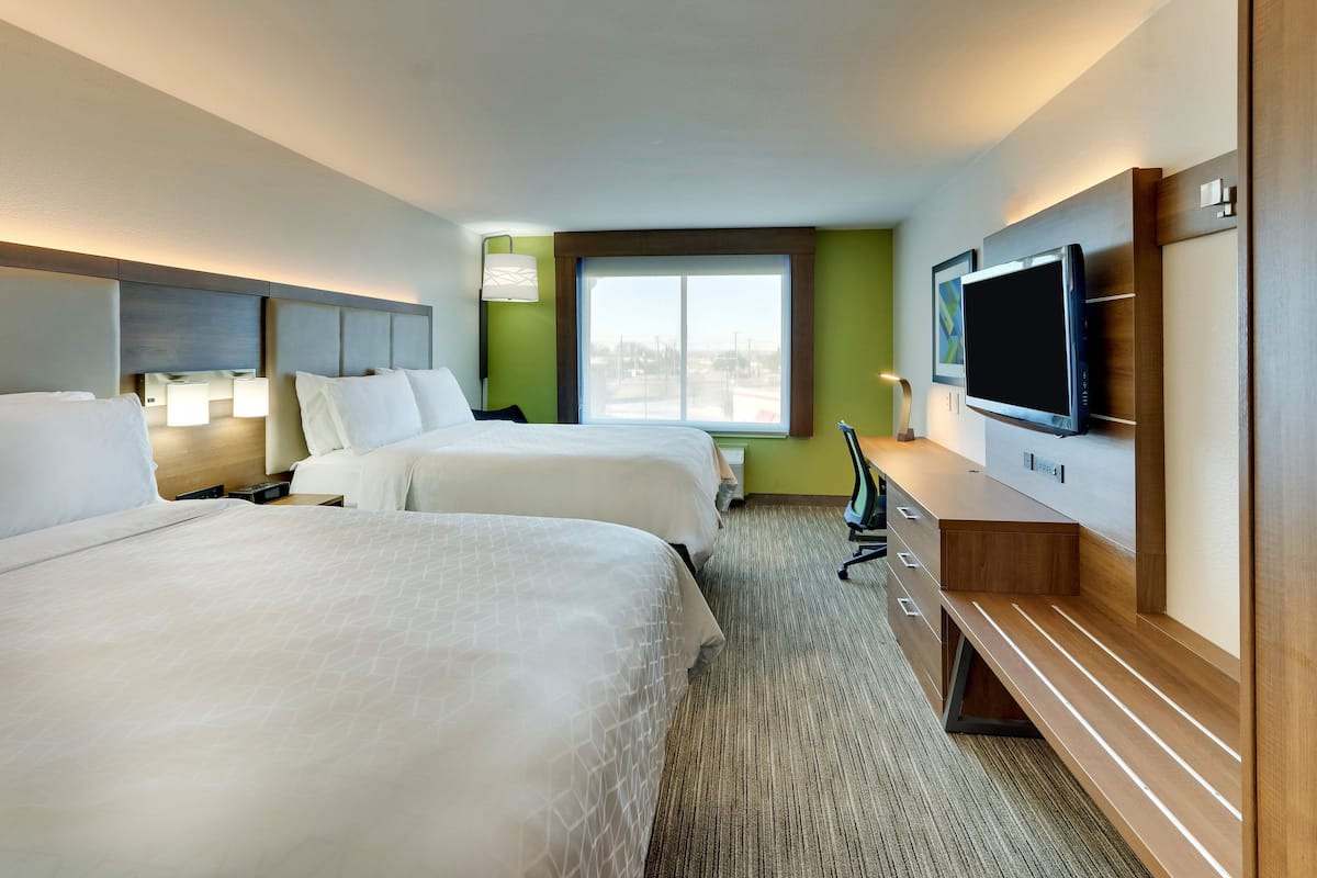 A hotel room with two beds, a TV, a desk, and a window with a view.