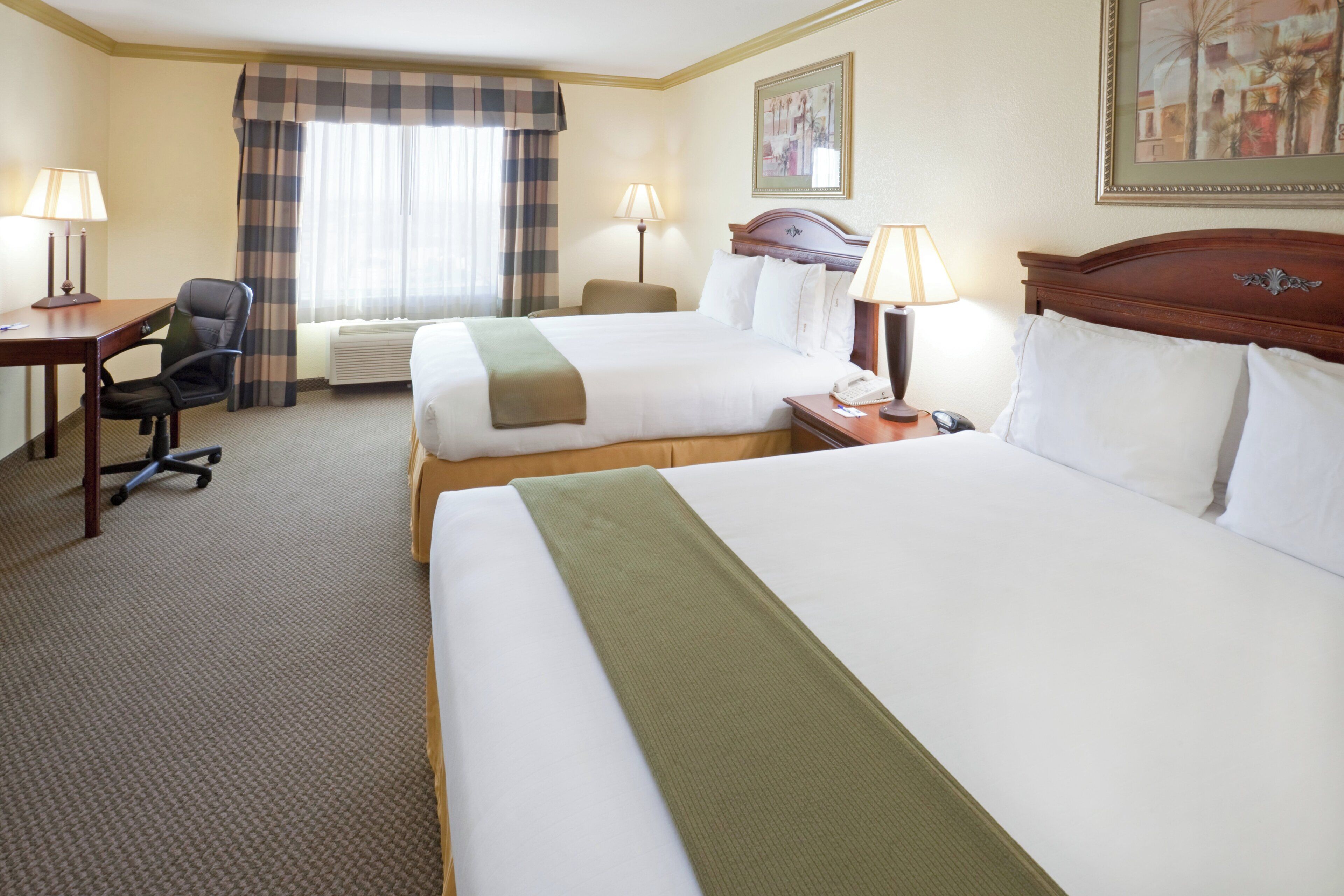 A hotel room with two beds, a desk, a chair, and a window with curtains.