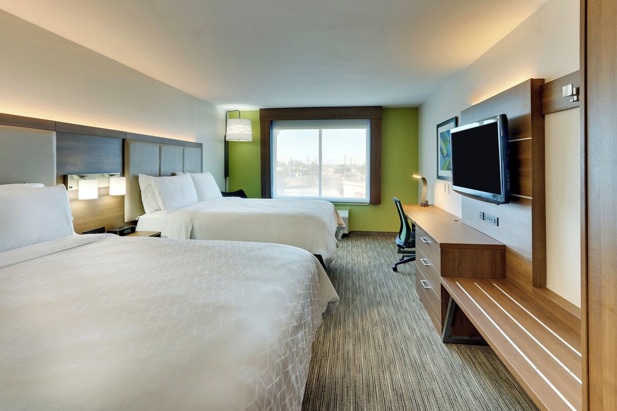 A hotel room with two beds, a TV, a desk, and a window with a view.