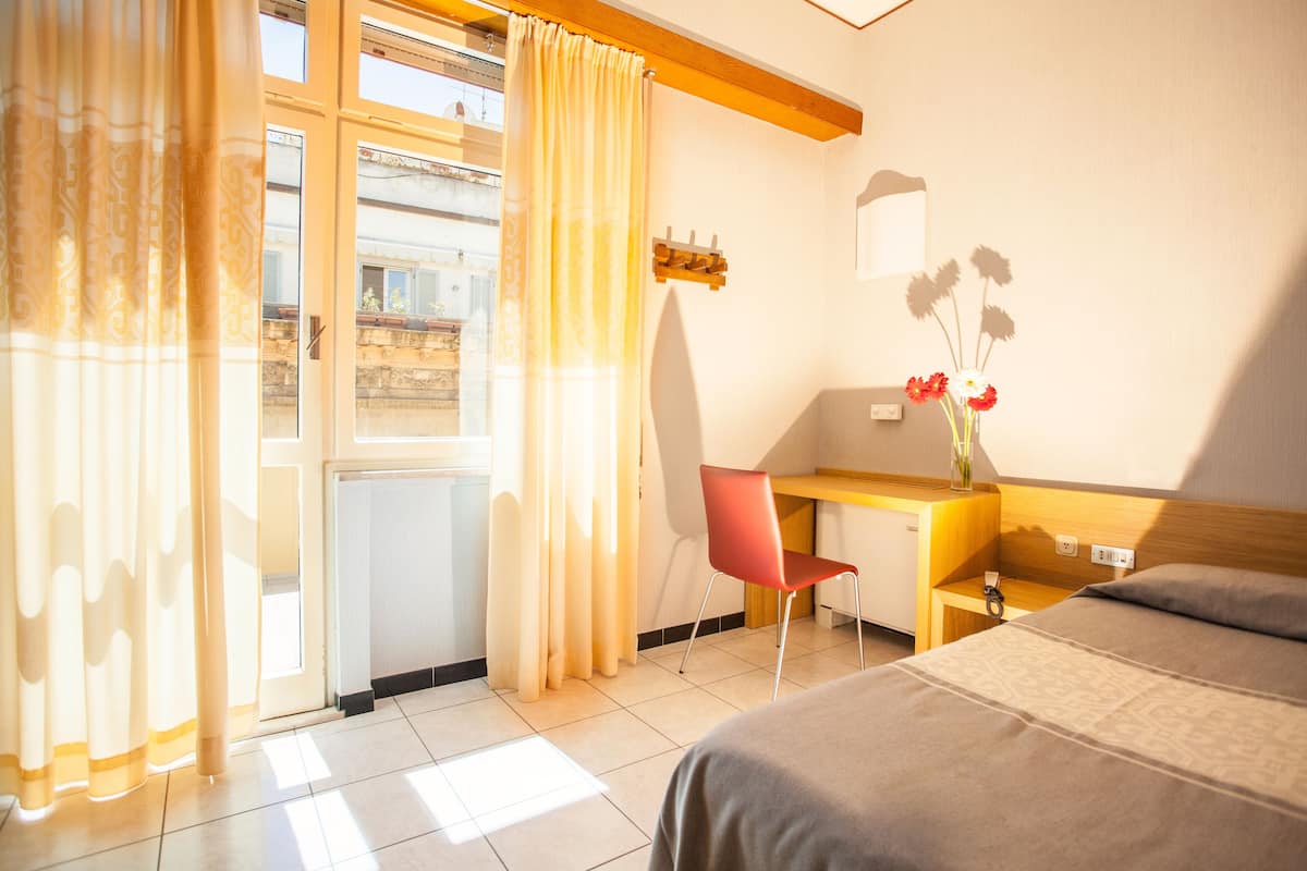 A hotel room with a bed, a desk, a chair, and a window with curtains.