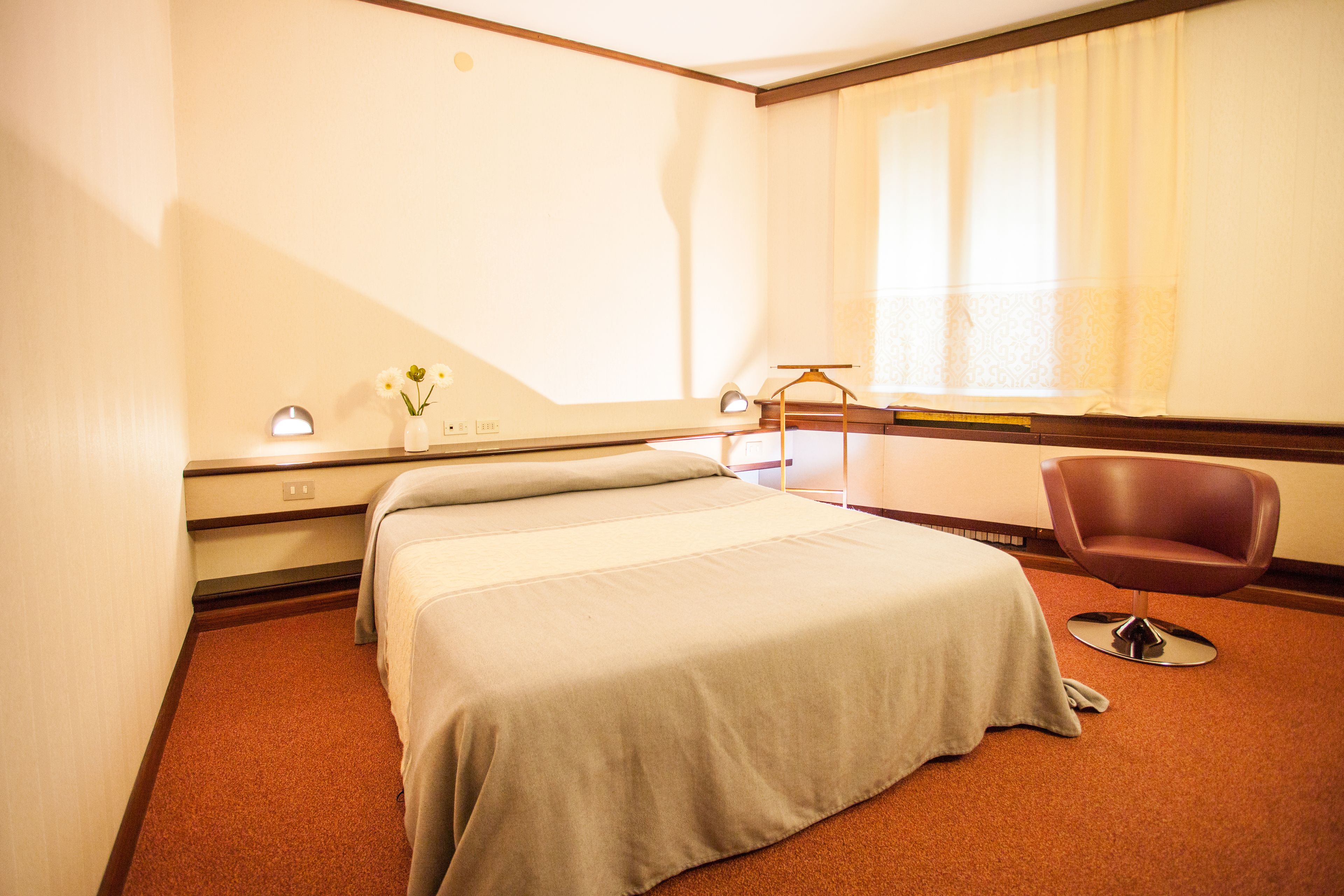 A hotel room with a bed, a chair, a desk, and a window with curtains.