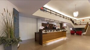 Un moderno hall de hotel con mostrador de recepción, una escalera y una planta en maceta grande.