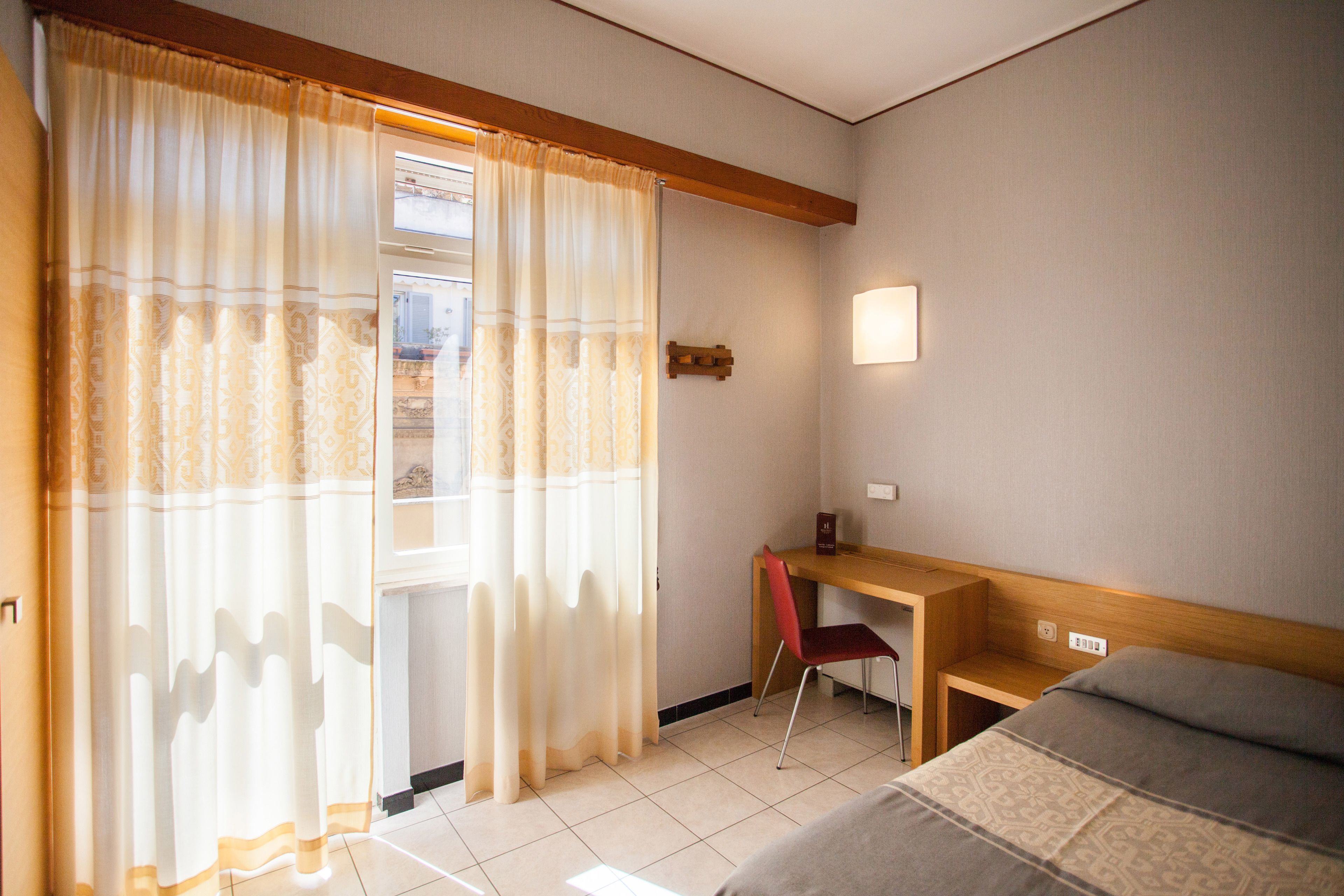 A hotel room with a bed, a desk, a chair, and a window with curtains.