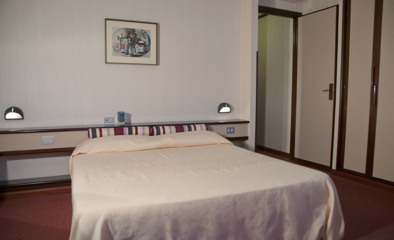 A hotel room with a bed, bedside lamps, a framed picture on the wall, and a wardrobe.
