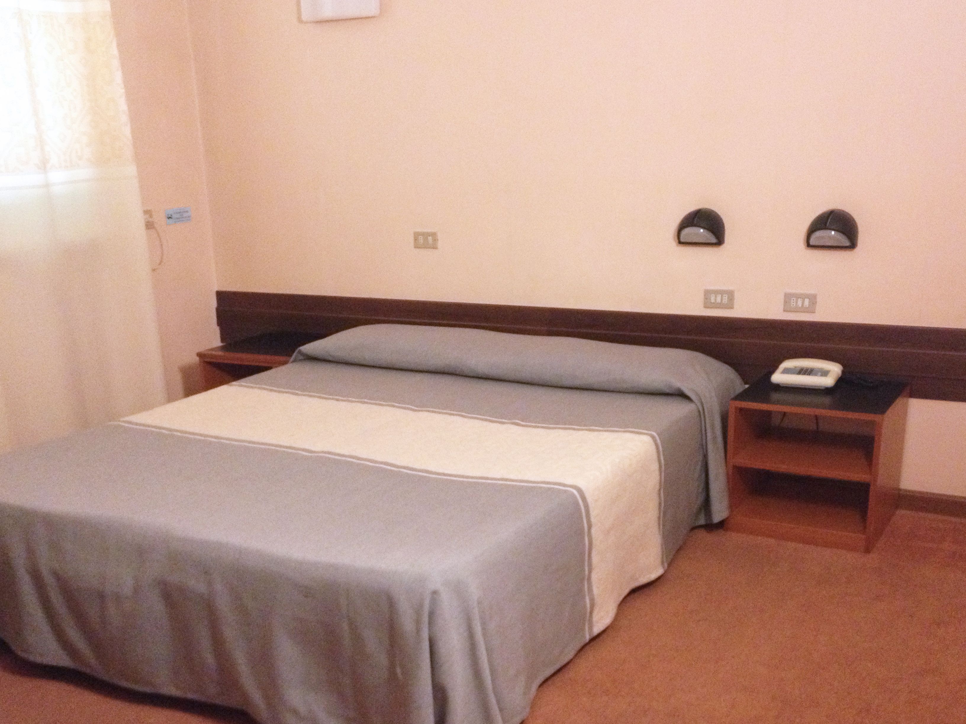 A hotel room with a bed, a bedside table with a phone, and a wall-mounted light fixture.