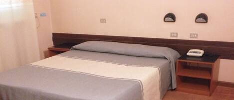 Una habitación de hotel con una cama, una mesita de noche con teléfono y una lámpara fijada a la pared.