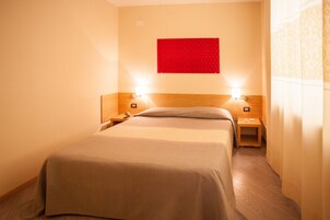 Una camera d'albergo con un letto, due comodini, un pannello decorativo rosso e una testiera in legno.