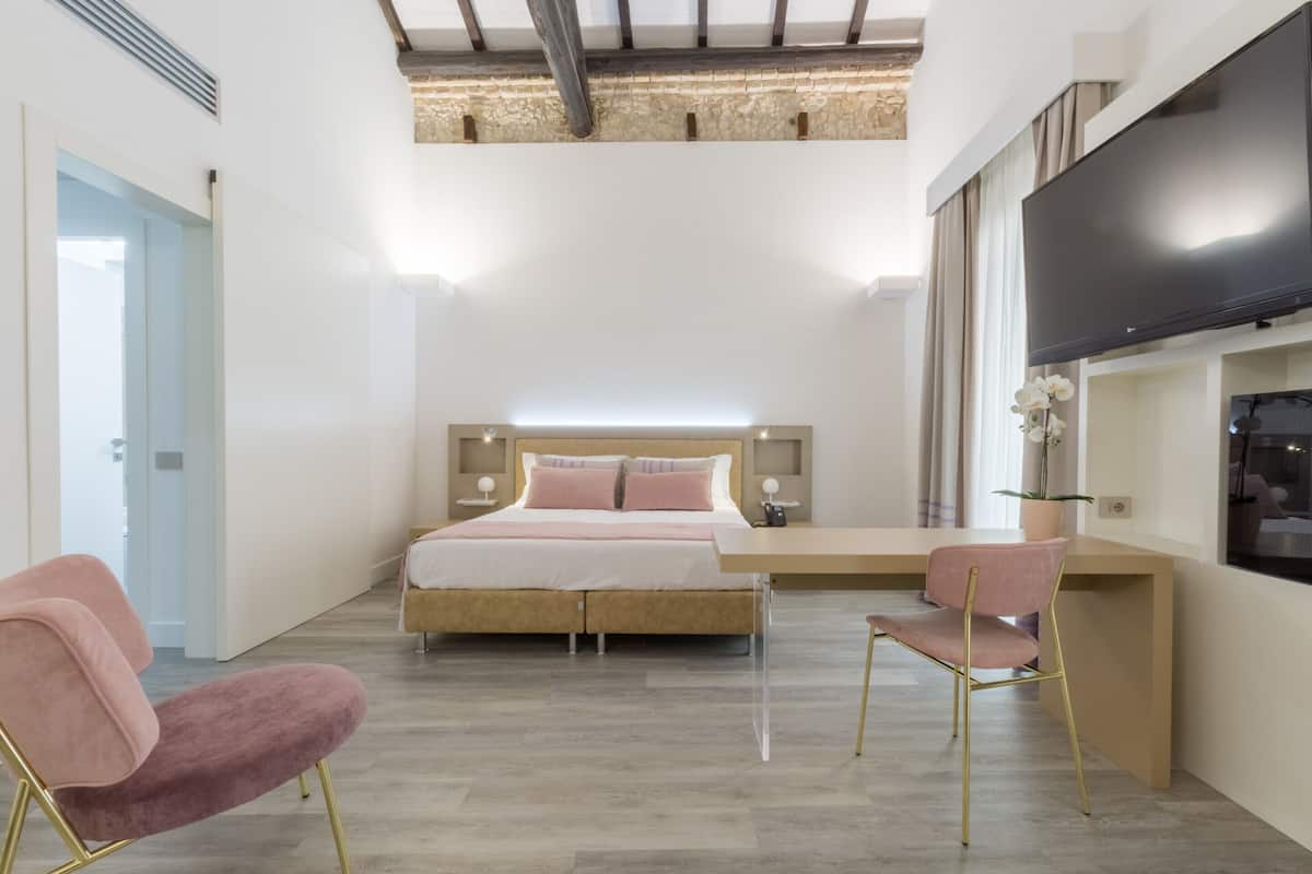 A bedroom with a bed, bedside tables, a TV, and a desk area.