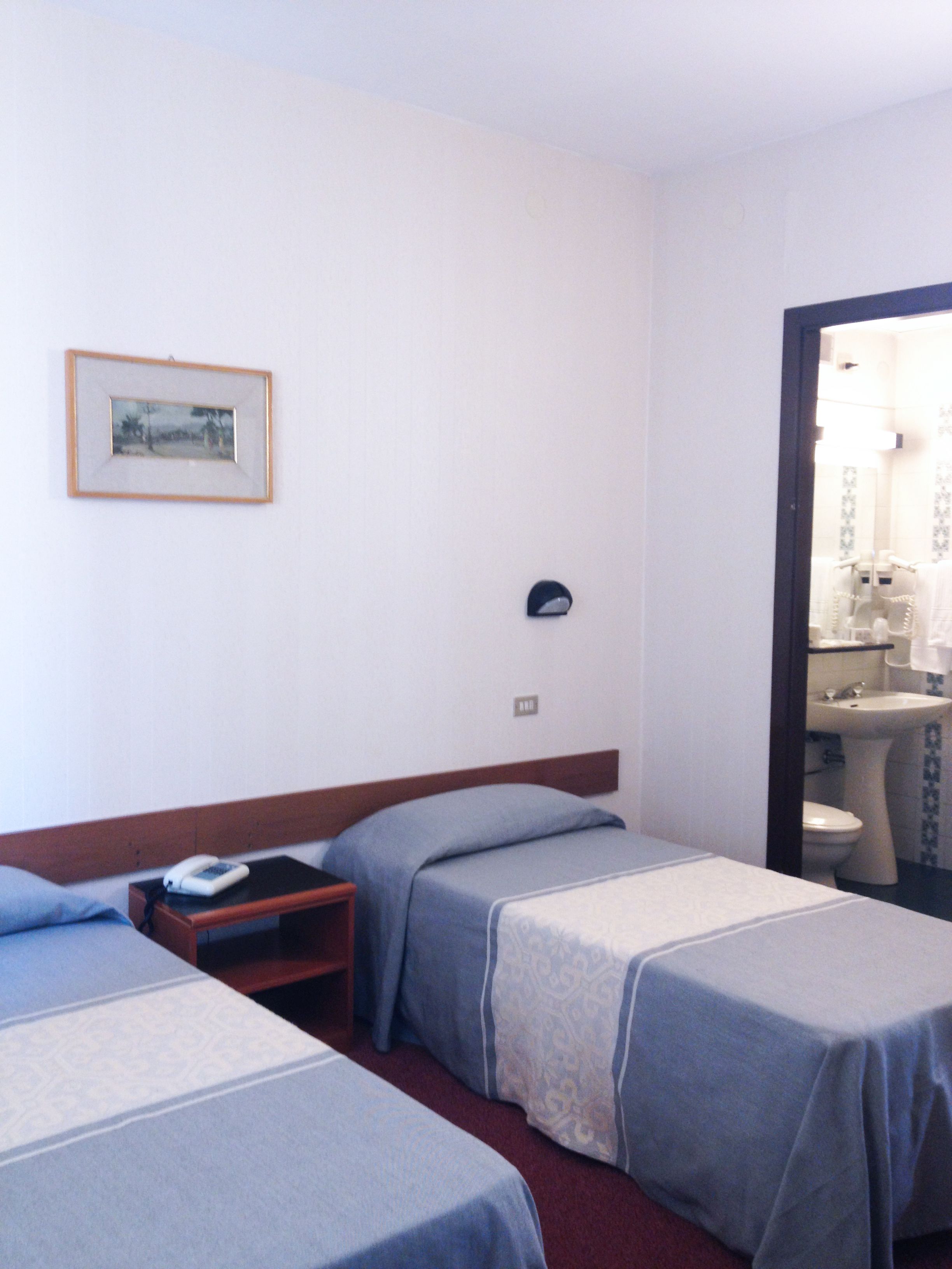 A hotel room with two single beds, a bedside table with a phone, a framed picture on the wall, and a bathroom visible through an open door.