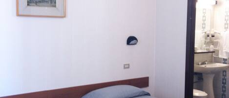 A hotel room with two single beds, a bedside table with a phone, a framed picture on the wall, and a bathroom visible through an open door.
