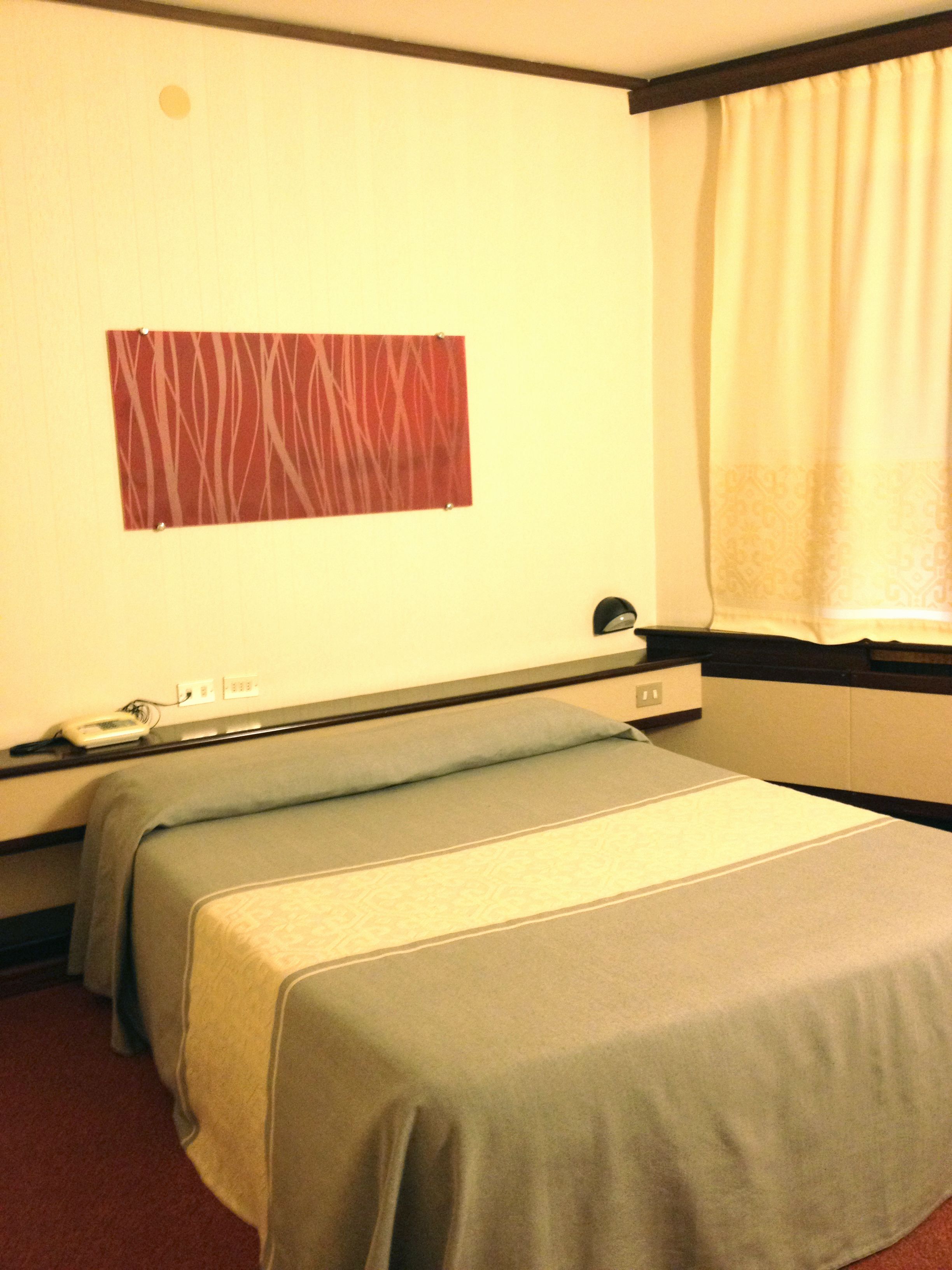 A hotel room with two single beds, a wall-mounted TV, and a window with curtains.