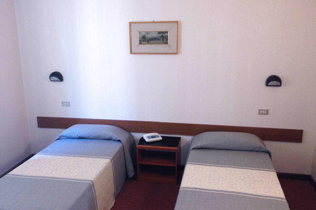 A hotel room with two single beds, a nightstand, a telephone, and a framed picture on the wall.